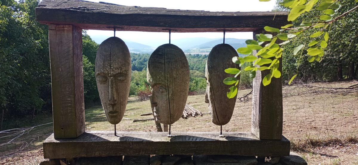 Dřevěné sochy hlav moai zavěšené v rámu s výhledem do krajiny